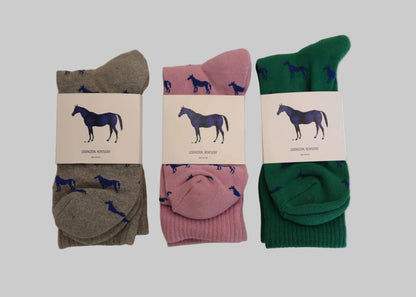 Three pairs of socks in gray, pink, and green with horse design labels on a beige background.