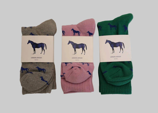 Three pairs of socks in gray, pink, and green with horse design labels on a beige background.